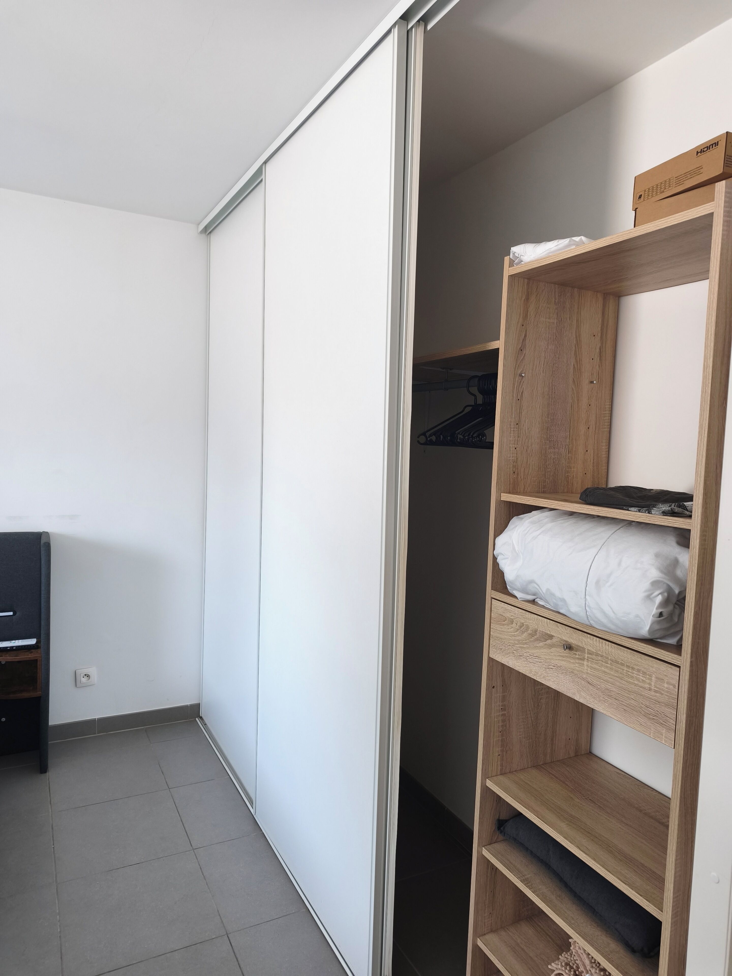 Une pièce avec un placard à porte coulissante, une étagère en bois et un téléviseur posé sur un meuble.