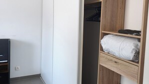 A room with a sliding door closet, a wooden shelf unit, and a television on a stand. - Two-bedroom apartment with a private garden, air conditioning, and two parking spaces. (Istres)