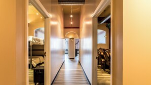 Un couloir d’hôtel avec un plancher en bois, des lits superposés et un coin repas avec des chaises.
