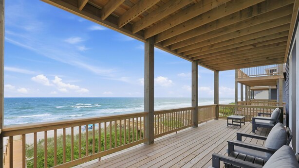 A wooden deck with a railing overlooking the ocean, featuring outdoor seating and a view of the beach. - Tide & Blue | Oceanfront Luxury, Pool, Sleeps 18 (Surf City)