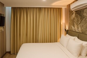 Une chambre d’hôtel avec un grand lit, des rideaux beiges, un téléviseur fixé au mur et un mur en marbre.