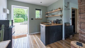 Une cuisine dotée d’un plan de travail en bois, d’étagères intégrées, d’une fenêtre et d’une porte donnant sur un espace extérieur.