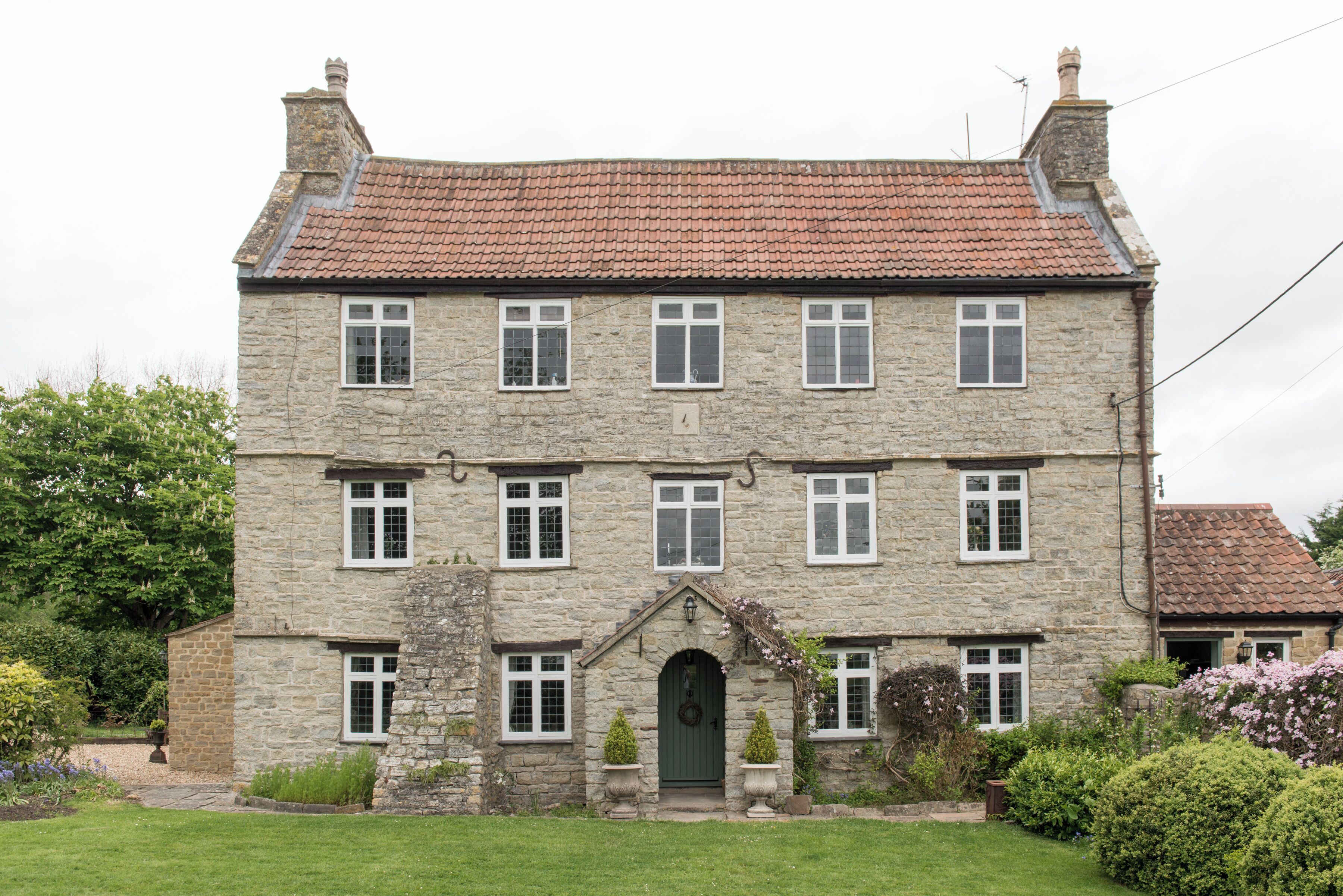 A stone building with a green door, multiple windows, and a red-tiled roof.
