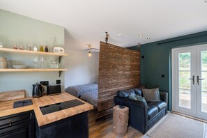 A compact living space with a kitchenette, a bed, a seating area, and a large window. - Cottage Poppy (Keynsham)