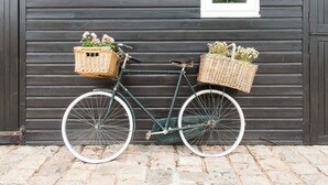 Uma bicicleta com cestas de vime em frente a uma parede de madeira.