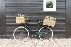 A bicycle with wicker baskets against a wooden wall. - Cottage Poppy (Keynsham)