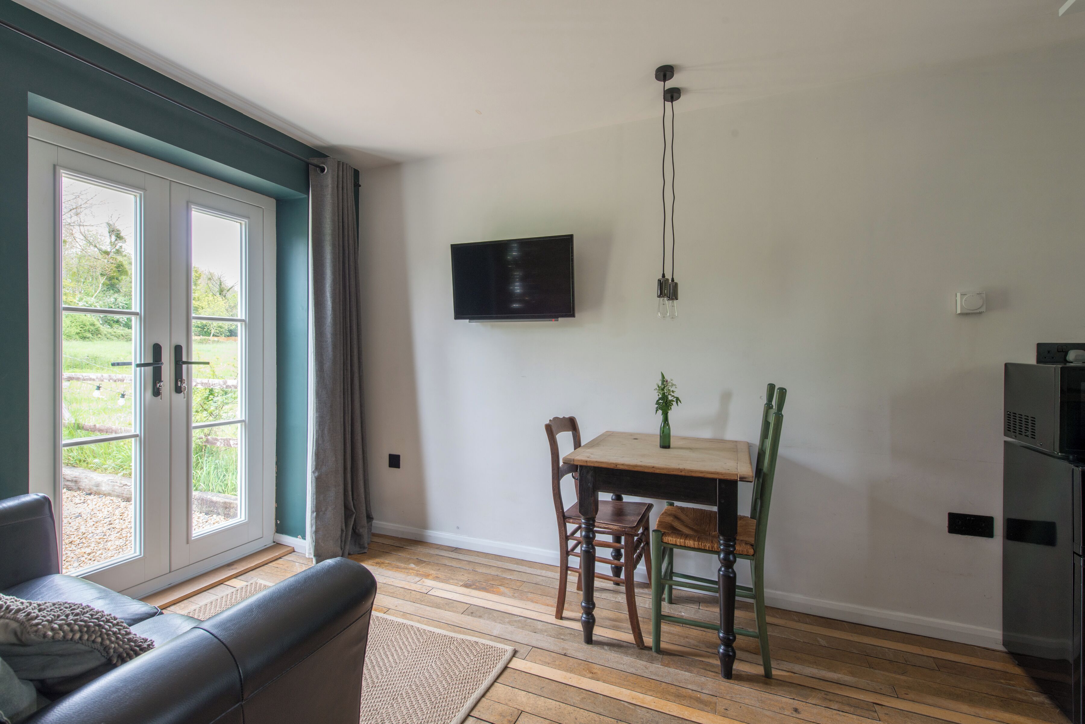 A room with a sofa, a dining table with chairs, a TV mounted on the wall, and a sliding glass door leading to an outdoor area.