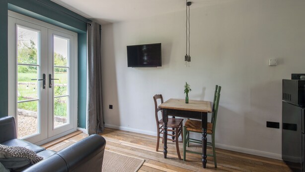Quarto com sofá, mesa de jantar com cadeiras, televisão fixada na parede e porta de vidro deslizante para área externa.