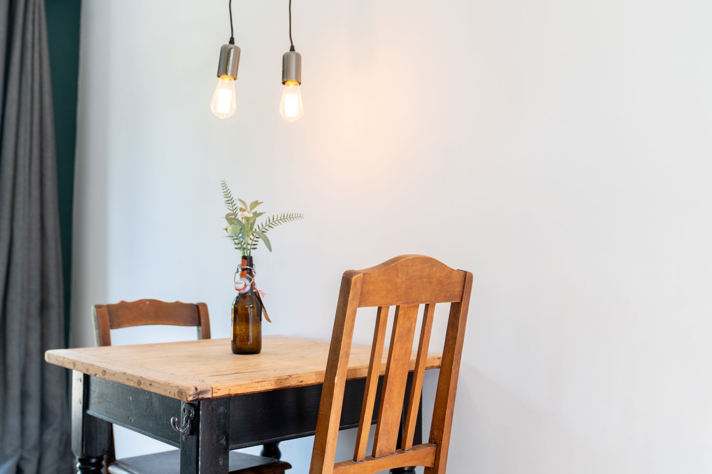 A wooden dining table with two chairs, a bottle of beer, and a plant on the table.