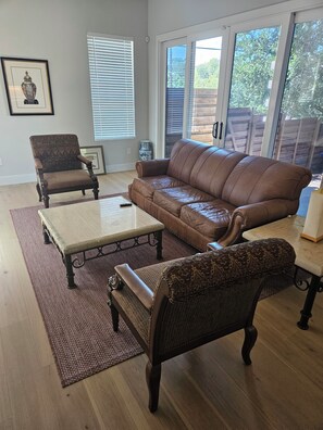 Ein Wohnzimmer mit braunem Ledersofa, zwei gemusterten Sesseln, einem Holztisch und einem roten Teppich.