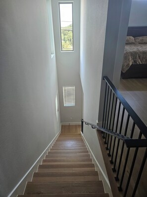 Una escalera con escalones de madera y barandilla metálica que lleva a un dormitorio con cama.
