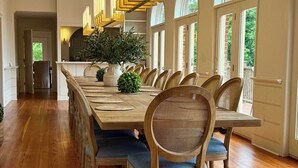 A dining area with a long wooden table, wicker chairs, and a modern pendant light fixture. - Private 16-Acre Lakefront Manor | Pool | Sleeps 14 (Culpeper)