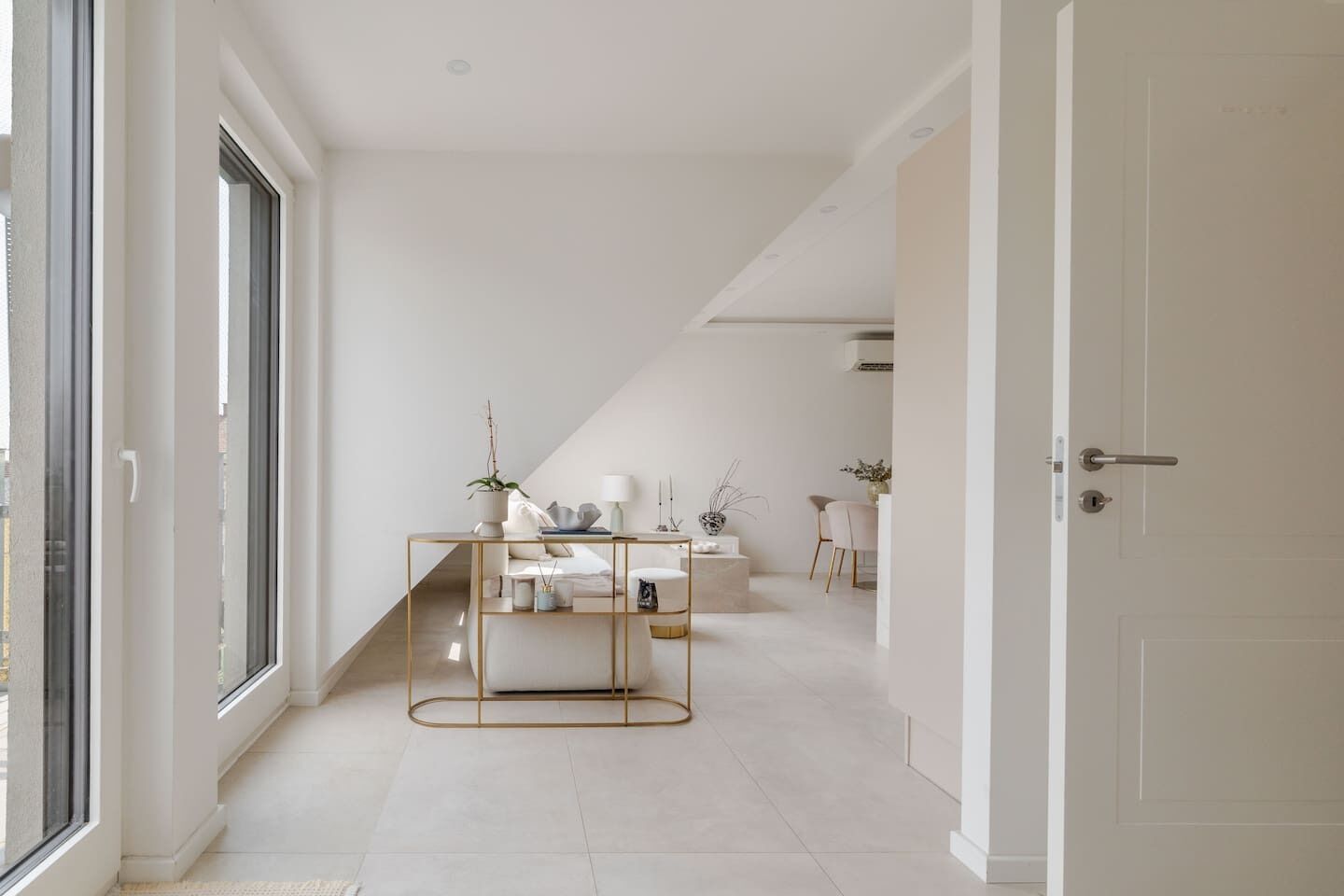 Ein modernes, minimalistisches Interieur mit einem zentralen Konsolentisch, einer weißen Tür und einem Ausblick durch ein großes Fenster.