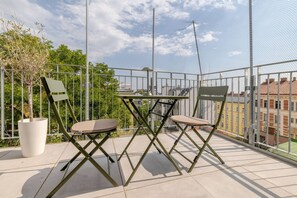 A balcony with a table and two chairs, a potted plant, and a view of buildings. - lux Rooftop with A/C - Schönbrunn & Central Vienna (Wien)