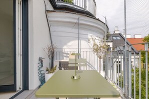 Ein moderner Sitzbereich im Freien mit Tisch und Stühlen, einem Metallzaun und einem Gebäude mit weißer Fassade und geneigtem Dach.