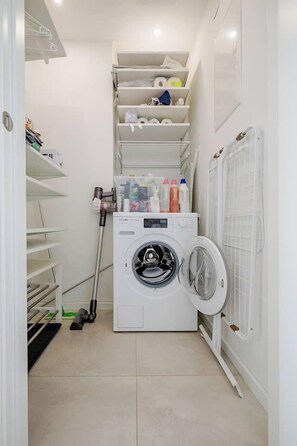 A laundry room with a washing machine, shelves with laundry supplies, and a vacuum cleaner. - lux Rooftop with A/C - Schönbrunn & Central Vienna (Wien)