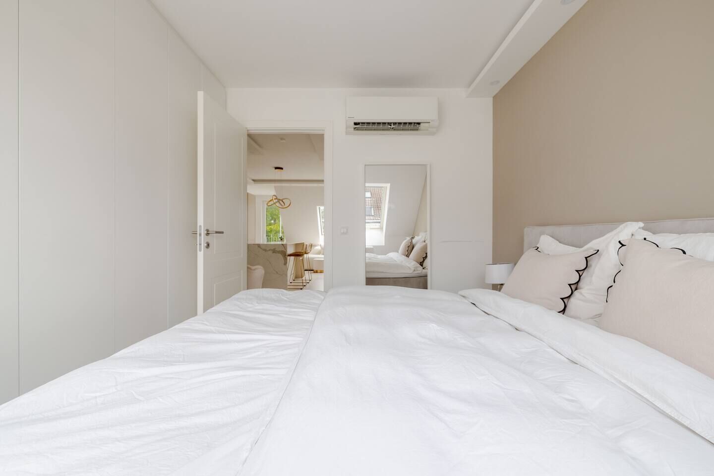 A bedroom with a large bed, a door leading to a bathroom, and a view of a dining area.