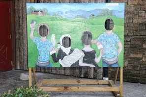 Una pintura sobre un caballete con un paisaje rural de fondo.