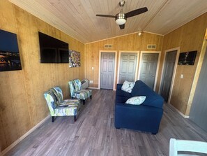 A room with a ceiling fan, a blue sofa, patterned armchairs, and a mounted TV.