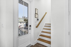 A white interior with a wooden staircase, a door with a window, and two framed certificates on the wall. - The Oasis • 3 Kings • Short Beach Walk • Elevator (Fort Myers Beach)