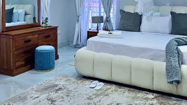 A modern bedroom with a large bed, a wooden dresser, a mirror, and a ceiling light fixture. -     Escape Ordinary at The Hill Manor - A Sanctuary of Luxury, Privacy & Comfort (Ndola)