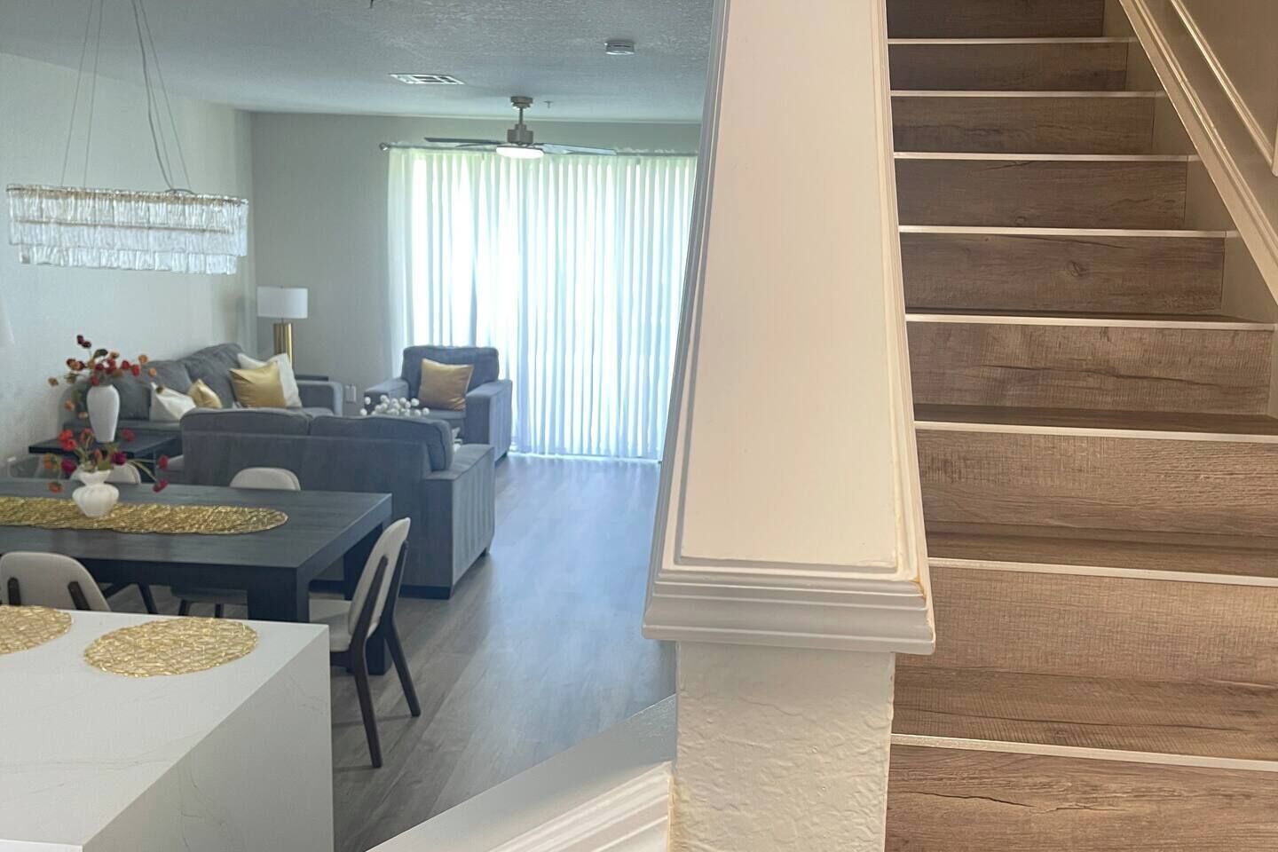 A staircase leading to a living area with a dining table and chairs, a sofa, and a ceiling fan.