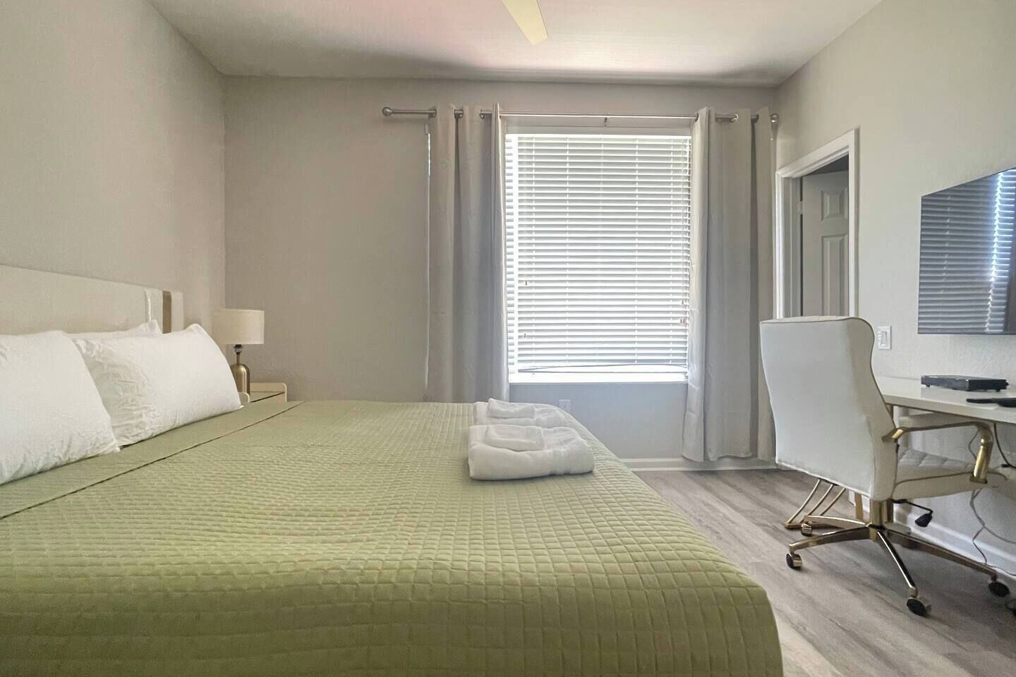 Una habitació d'hotel amb llit, escriptori, cadira i finestra amb persianes.