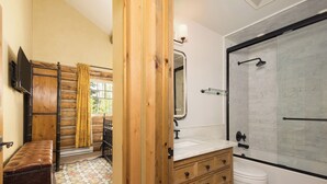 Baño con banco de madera, lavamanos con espejo, inodoro y zona de ducha.