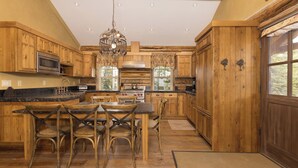Cocina con armarios de madera, una isla central con sillas, una lámpara colgante y un ventanal grande.