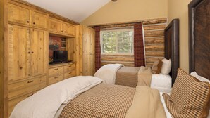 Una habitación con armarios de madera, un televisor, dos camas con ropa de cama a cuadros y un ventanal con cortinas.