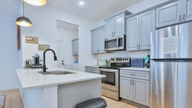 A modern kitchen with white cabinets, stainless steel appliances, a central island, and a trash bin.