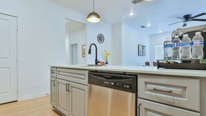 A modern kitchen with a dishwasher, cabinets, a ceiling fan, and a clock on the wall.