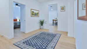 A spacious hallway with a patterned rug, a dining area with chairs and a table, and a ceiling fan.