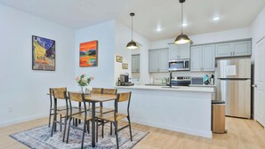 A modern kitchen with a central island, pendant lighting, and a dining area with a rug.