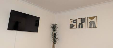 Una habitación con una televisión de pantalla plana montada en la pared, una planta en maceta y tres cuadros abstractos enmarcados.