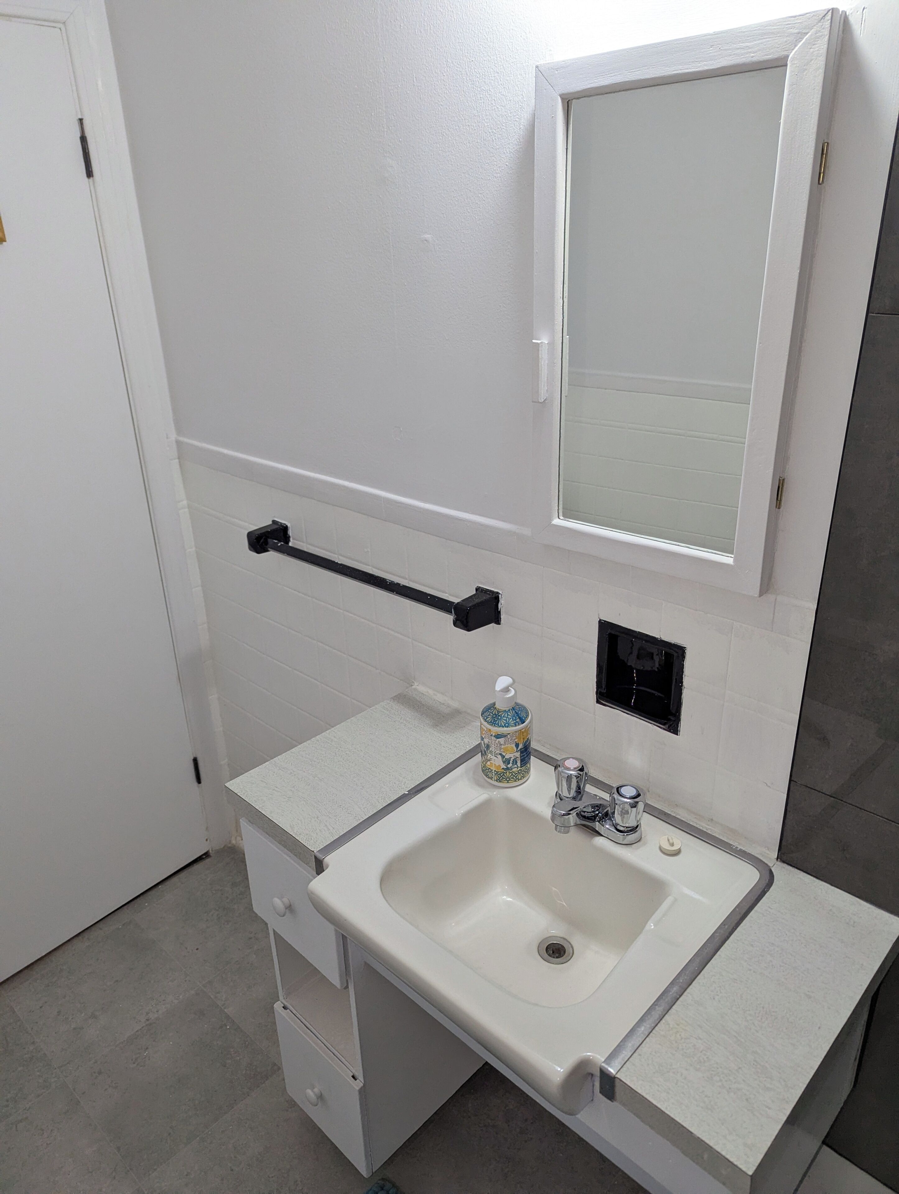 A bathroom with a white sink, a mirror, a towel rack, and a soap dispenser.