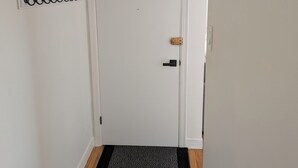 Une porte blanche avec un paillasson noir, un panneau à crochets fixé au mur et un plancher en bois.