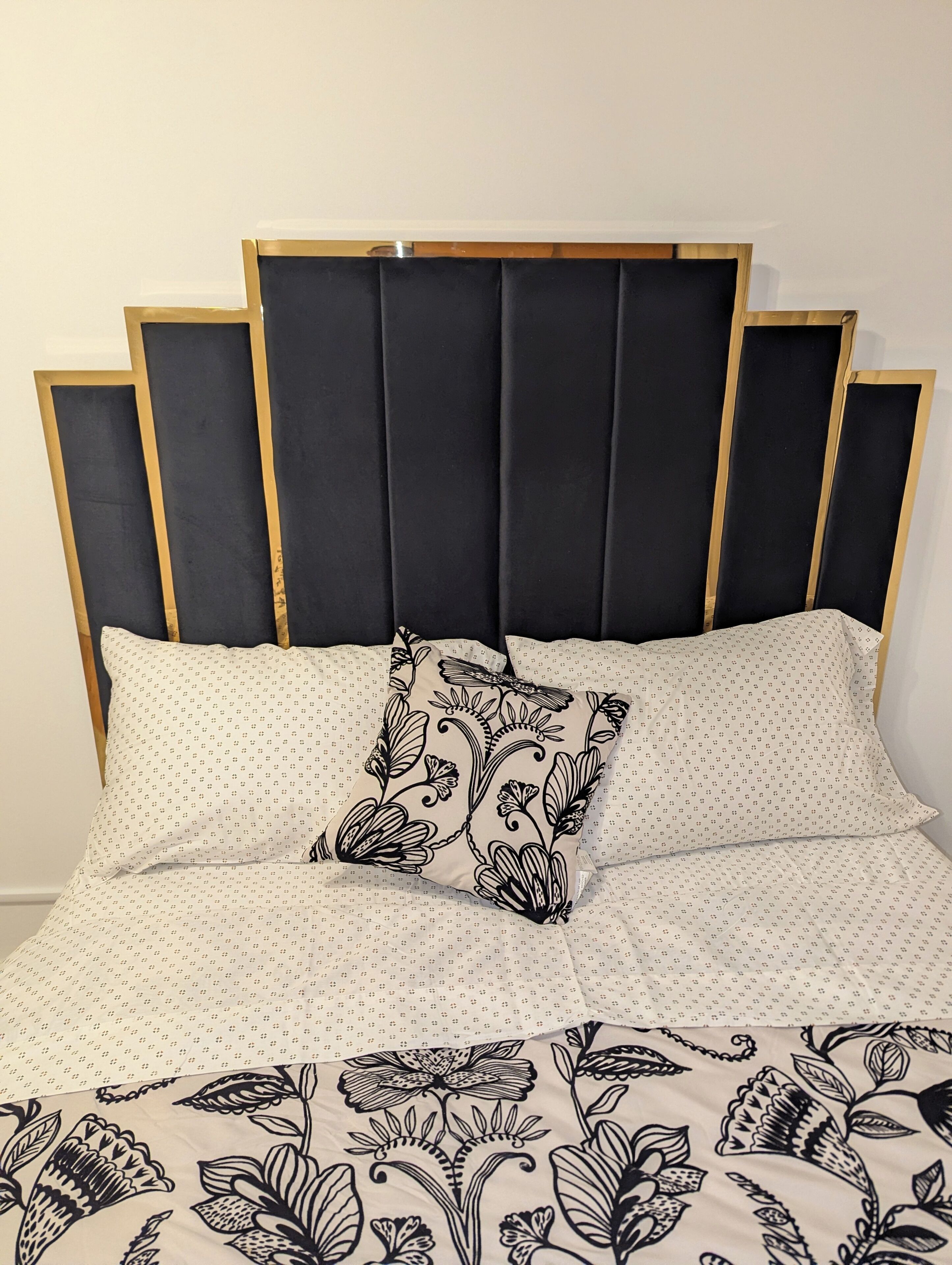 Ein Bett mit einem gemusterten Bettüberwurf, einem Zierkissen und einem Kopfteil mit vertikalen Leisten.
