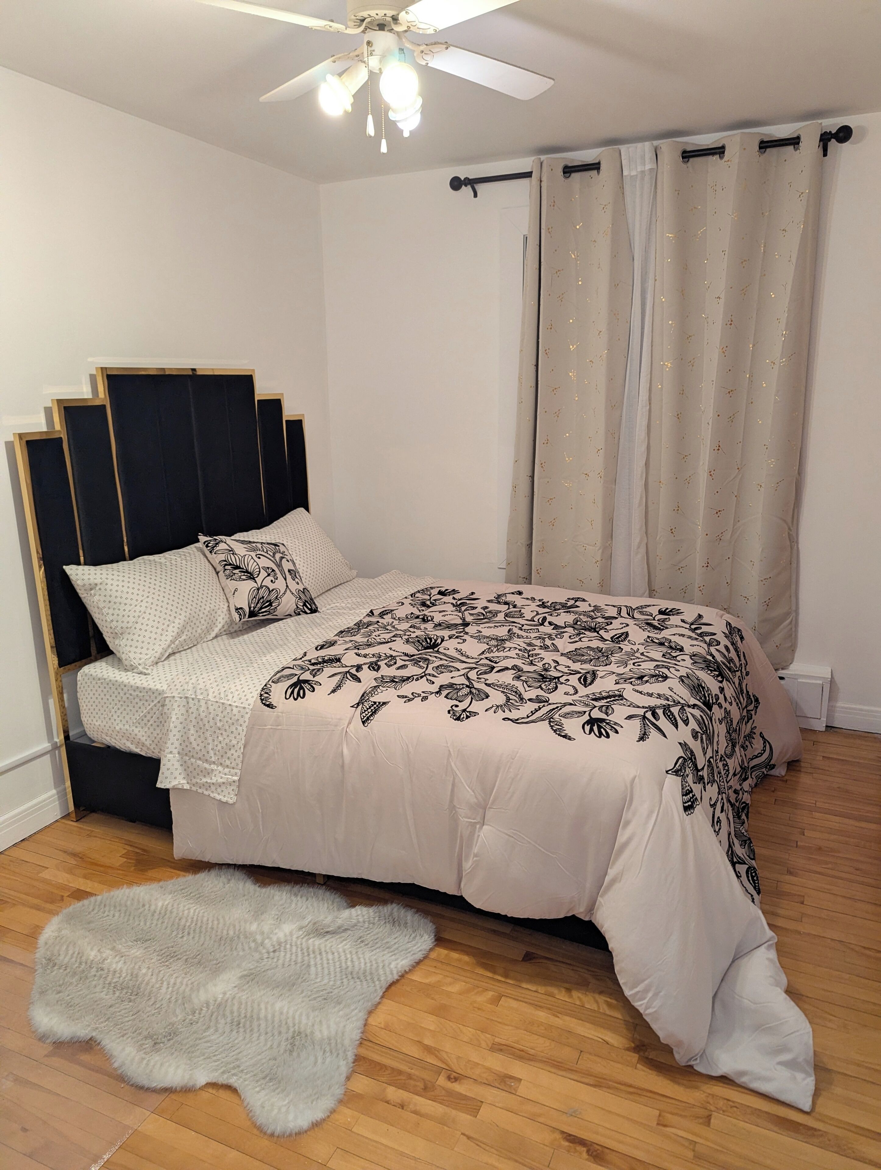 Une chambre à coucher avec un lit, un ventilateur de plafond et une fenêtre avec des rideaux.
