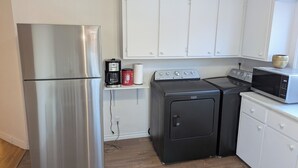 Une cuisine compacte équipée d’un réfrigérateur en acier inoxydable, d’un lave-linge, d’un four à micro-ondes et d’une machine à café, le tout placé sur une petite étagère.