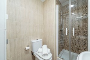 Een badkamer met toilet, een douchecabine van glas en beige betegelde wanden.