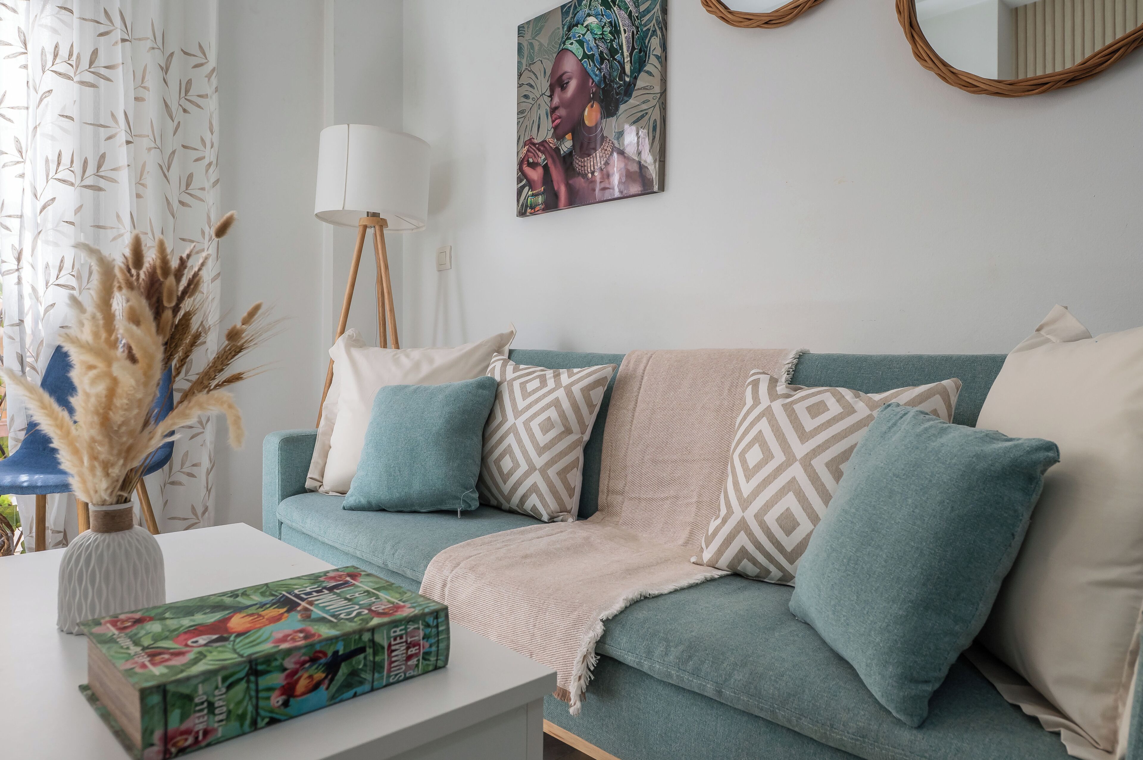 Ein Wohnzimmer mit einer Couch, dekorativen Kissen, einer Vase mit Trockenpflanzen, einer Lampe und einem Bild an der Wand.