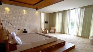 A modern bedroom with a large bed, a wooden headboard, a flat-screen TV, and a view of a garden through large windows. - Villa D'horizon (Marrakech)