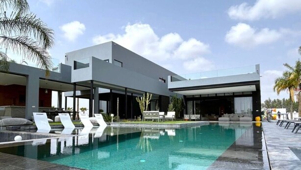 A modern pool area with a rectangular pool, lounge chairs, and a contemporary building with large windows. - Villa D'horizon (Marrakech)