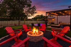 A backyard with a fire pit, red Adirondack chairs, a pool, and a covered patio area.