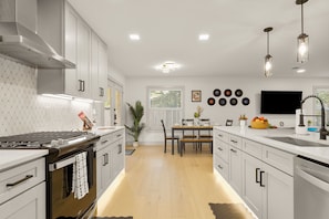 A modern kitchen with white cabinetry, a built-in oven, a dining area with a table and chairs, and pendant lighting.