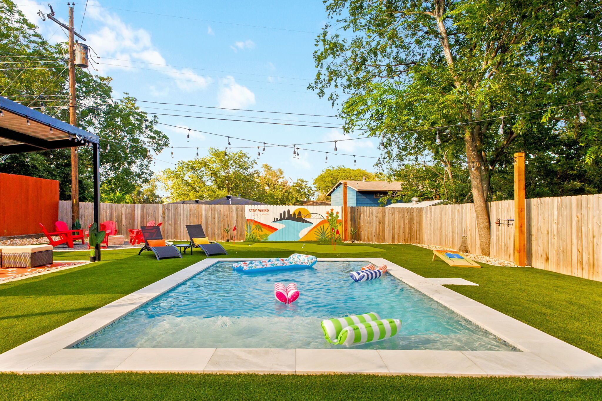 A backyard with a swimming pool, inflatable toys, and a wooden fence.