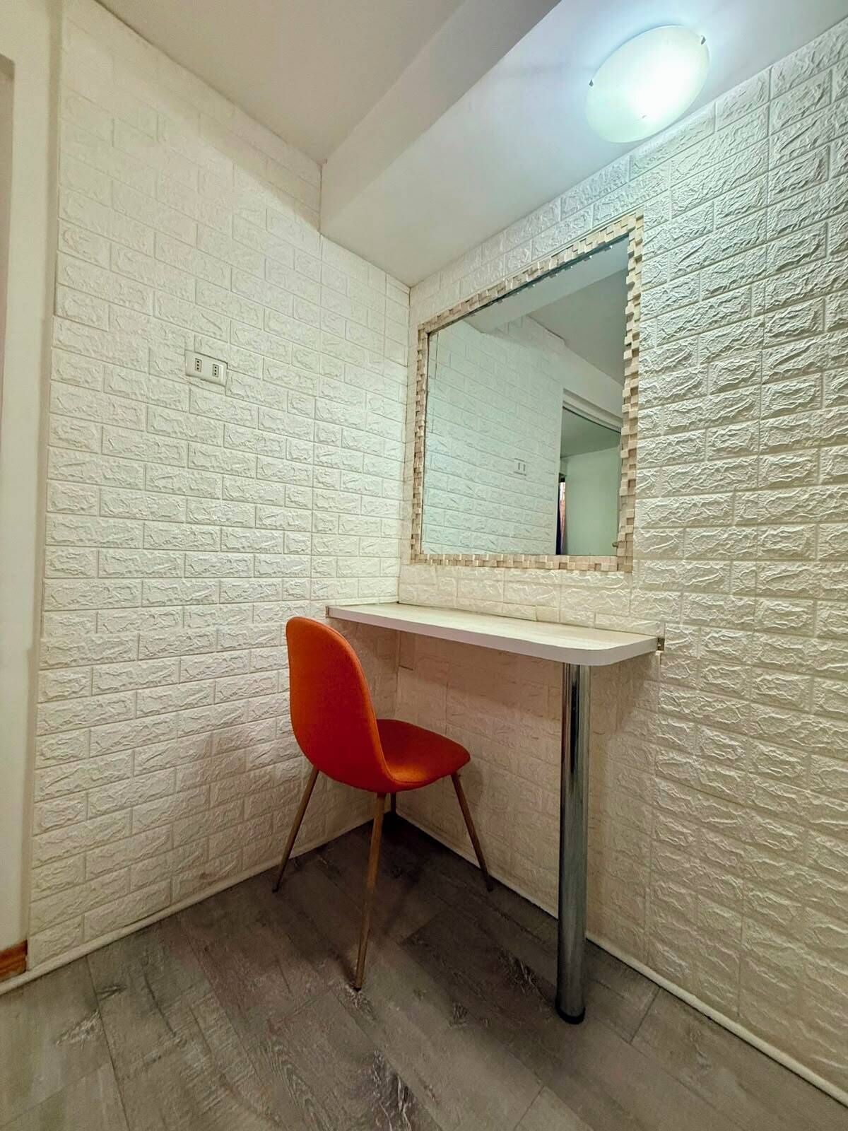 A corner room with a white brick wall, a mirror, a red chair, and a wooden floor.