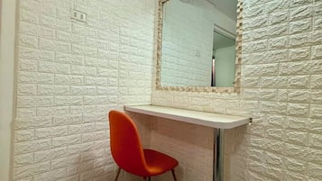 A corner room with a white brick wall, a mirror, a red chair, and a wooden floor.