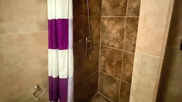 Une douche avec un rideau violet et blanc, des murs carrelés et un drain visible.